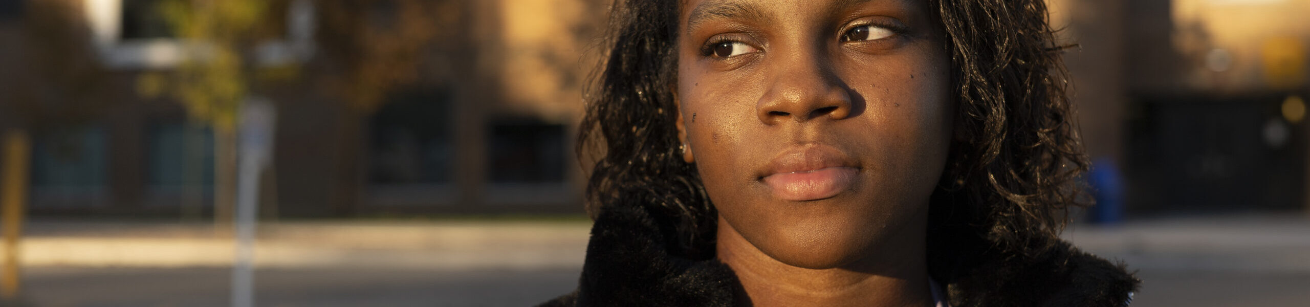 Woman in a black coat looking to her right as the sun sets.